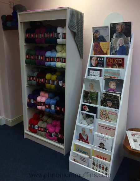 Red Heart yarns and books in the Bluestocking Wool Shop. A rack of books and some Red Heart yarns.